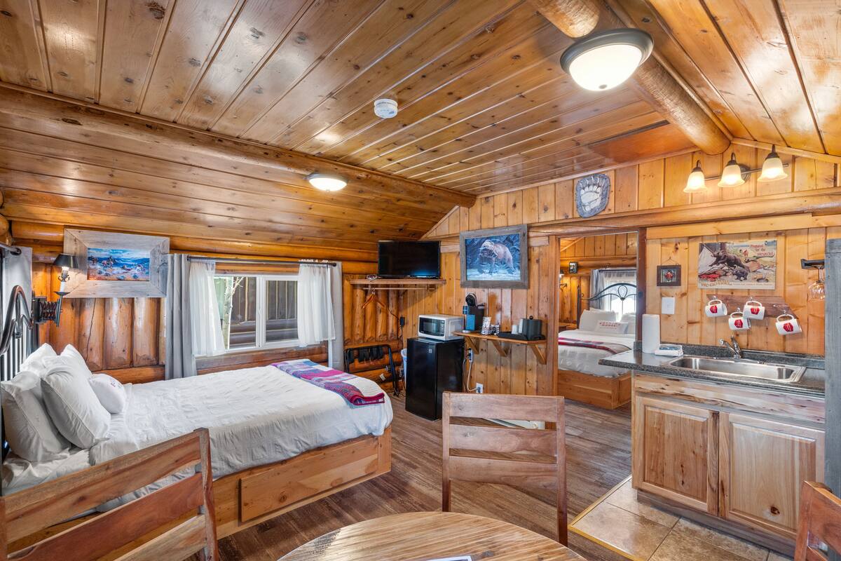 Una cabaña de madera con una cama, una mesa de comedor, una zona de cocina y un televisor.