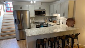 A modern kitchen with stainless steel appliances, a granite countertop, and bar stools.