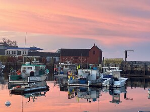 A marina with boats docked, a red building, and a calm water surface reflecting the surroundings. - Rockport Getaway near ocean, music hall & downtown (Rockport)