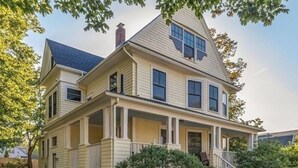 A two-story house with a front porch, a chimney, and a staircase leading to the entrance.