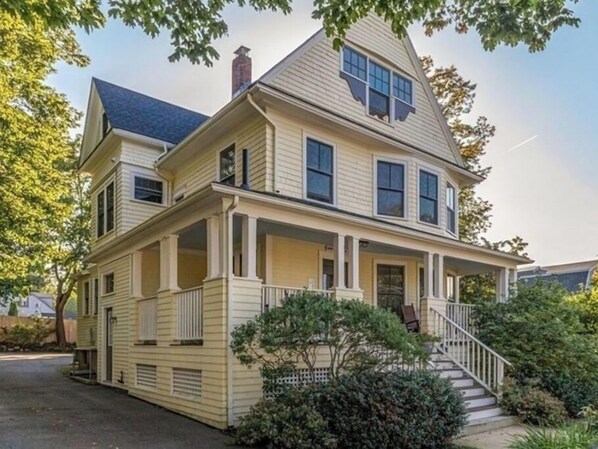 A two-story house with a front porch, a chimney, and a staircase leading to the entrance.