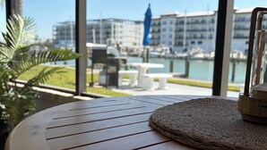 A round wooden table with a woven placemat, a potted plant, and a view of a marina with boats and buildings in the background. - Newly Remodeled. Water views from your private lanai.  Steps to Madeira Beach. (Madeira Beach)