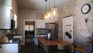 Kitchen features a central island with a gas stove and sink, surrounded by rustic brick walls and modern appliances.