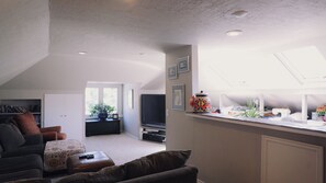 Relax in a spacious living area with a sofa, ottoman, and TV, surrounded by a bookshelf filled with books.