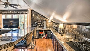 A spacious living area with a large TV, a ceiling fan, and a kitchen with marble countertops and a bar area. - Greenville Apt w/ Patio: Work, Play & Unwind! (Greenville)