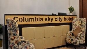 A reception desk at Columbia Sky City Hotel with a sign, two upholstered chairs with floral patterns, and a small potted plant. - columbia sky city (Cairo)