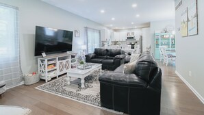 Ein modernes Wohnzimmer mit einem großen Flachbildfernseher, zwei schwarzen Ledersofas, einem weißen Couchtisch und einem gemusterten Teppich.