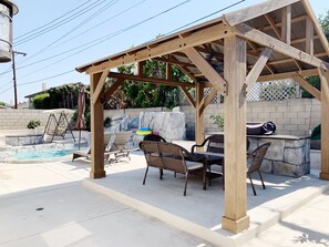 A wooden pergola with outdoor seating and a stone barbecue area.