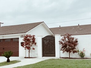 A residential house with a garage, a decorative metal gate, and two trees with red foliage.