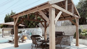 Una pérgola de madera con una barbacoa de piedra y zona de estar.
