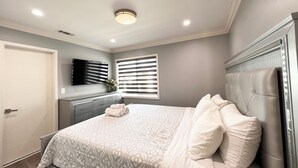 Un dormitorio con cama, cómoda, televisor y ventana con persianas.