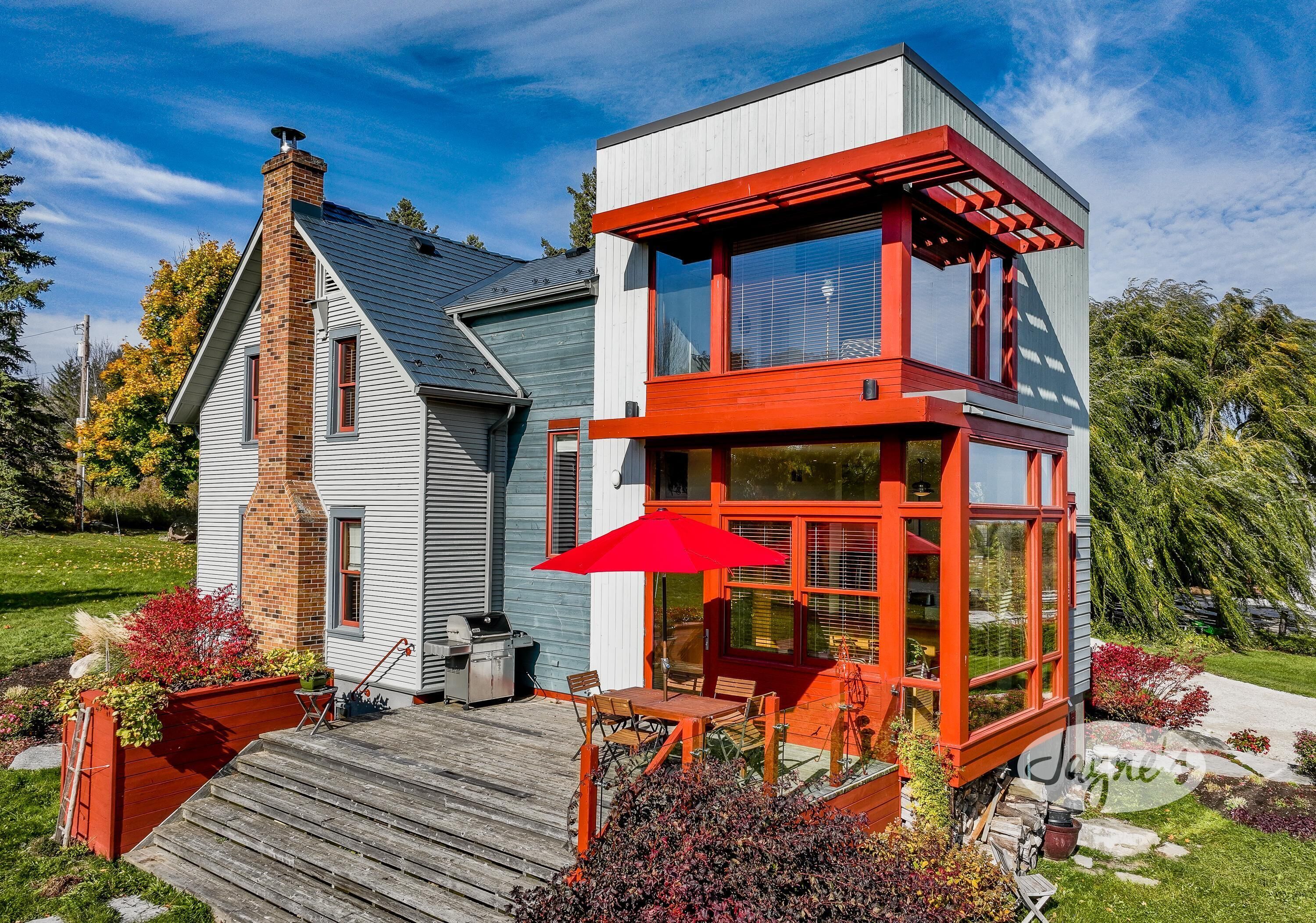 Une maison moderne avec une terrasse en bois, un parasol rouge et une cheminée en briques.