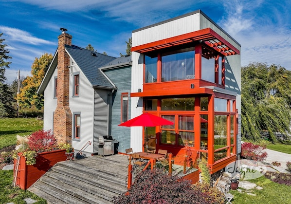 A modern house with a wooden deck, a red umbrella, and a brick chimney.