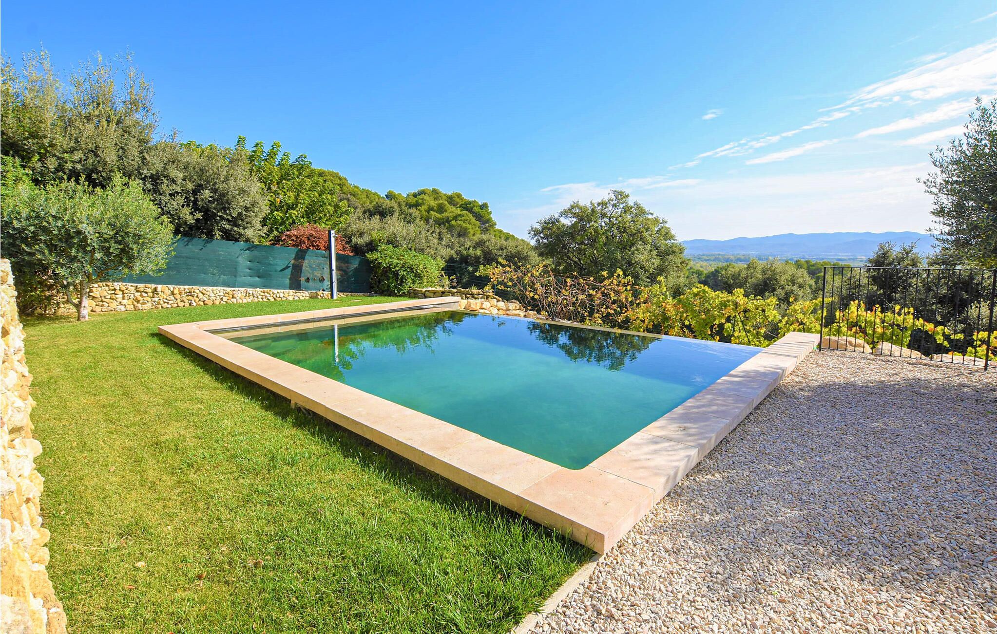 A rectangular pool with a stone border, surrounded by a well-maintained lawn and gravel area, with a backdrop of trees and a distant mountain range.