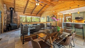 A log cabin interior with a stone fireplace, a dining area with a glass table, and a kitchen with modern appliances. - 2 cabins-22 guests-2 hot tubs-Lake Access-Glamping (Twain Harte)