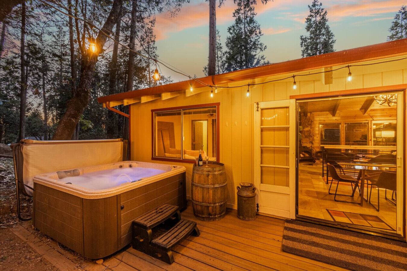 Une cabane en bois dotée d’un bain à remous, d’une terrasse en bois et d’un coin repas offrant une vue sur la forêt.