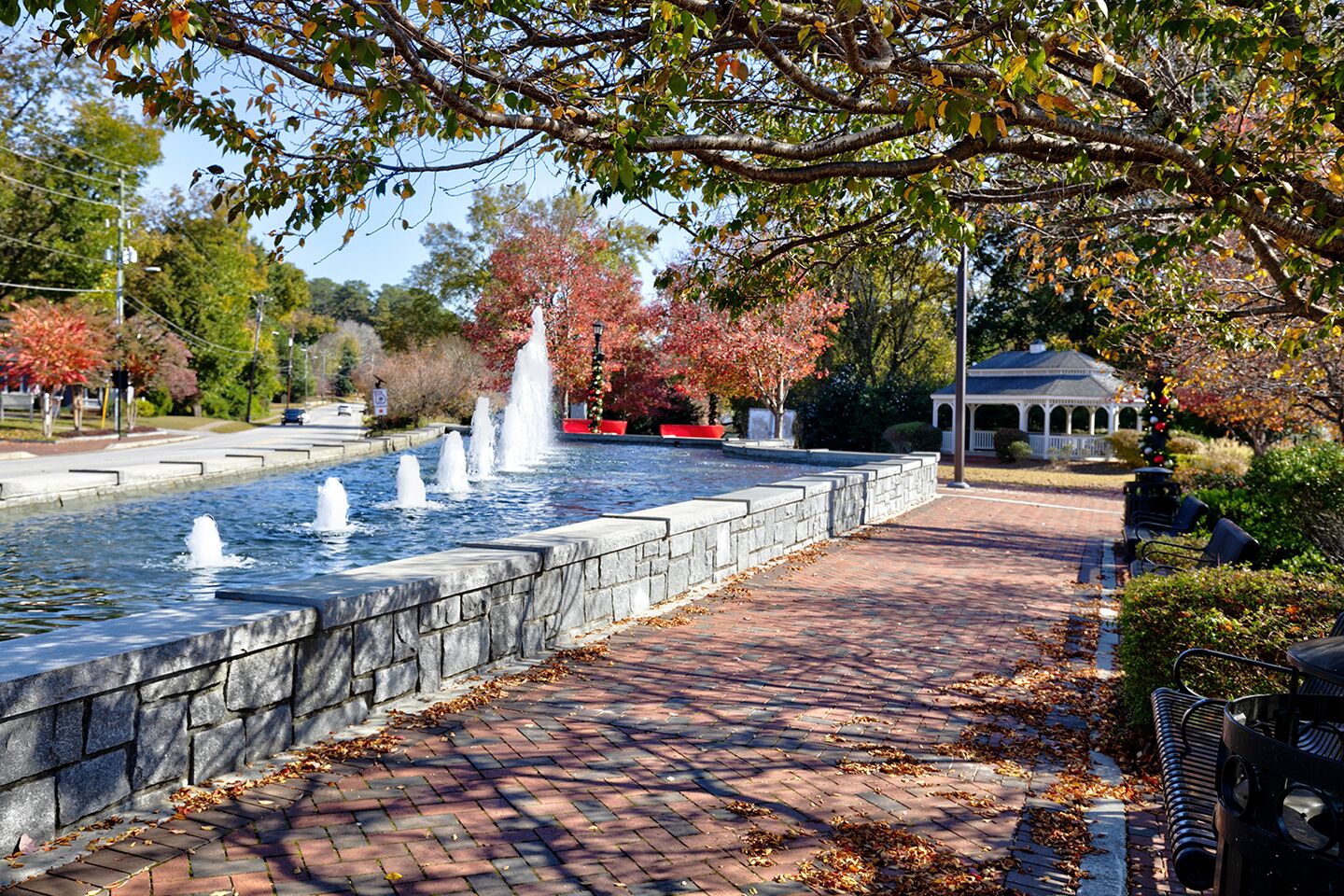 A fountain with water jets, surrounded by a stone wall and a brick pathway.