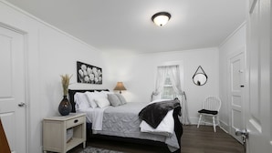 A bedroom with a bed, bedside table, lamp, chair, and a decorative wall piece. - Charming Country Cottage Retreat -  Walking distance to Downtown (Dallas)