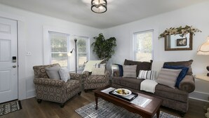 A living room with two patterned armchairs, a brown sofa, a wooden coffee table, and a large plant. - Charming Country Cottage Retreat -  Walking distance to Downtown (Dallas)