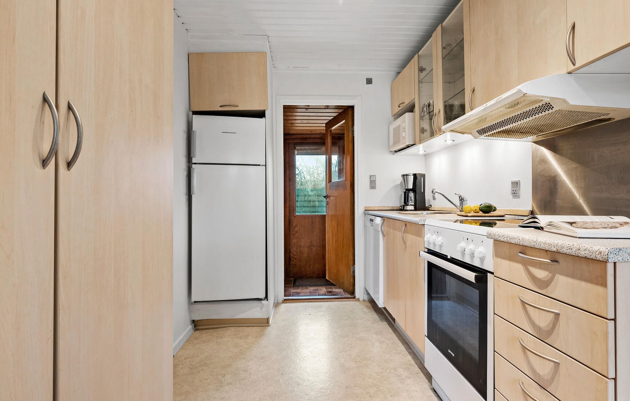 Une cuisine étroite avec des meubles de rangement en bois, un réfrigérateur blanc, une cuisinière et une machine à café.