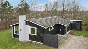 Une petite cabane à un seul étage, à l’extérieur sombre, avec une cheminée et une fenêtre.