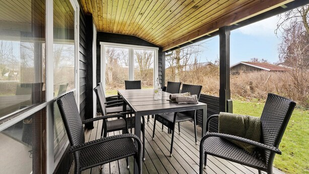 Un espace extérieur aménagé, abrité et doté d’une table et de chaises, de grandes fenêtres et d’une vue sur le paysage environnant.