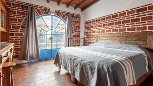 A bedroom with a brick wall, a wooden headboard, a bed with a striped bedspread, and a window with a blue frame.