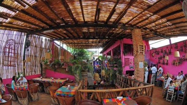 An outdoor restaurant with bamboo roofs, wicker furniture, and colorful tablecloths.