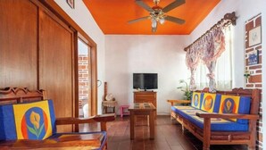 A living room with wooden furniture, a ceiling fan, a television, and a brick wall.