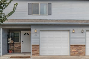 A two-story house with a white garage door, a front door with a number '653', and a small porch with a potted plant and a decorative item. - Tranquility: Spacious Townhome Near It All (Grand Junction)