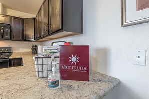 A kitchen with dark cabinets, a microwave, and a countertop with a bottle of hand sanitizer and a red box labeled "VISIT FRUITA Property Management". - Tranquility: Spacious Townhome Near It All (Grand Junction)