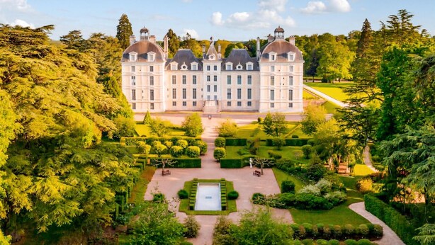 Een groot, klassiek gebouw met symmetrische architectuur, omgeven door verzorgde tuinen en bomen.