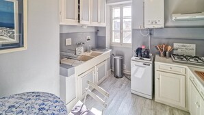 Een compacte keuken met witte kasten, een inbouwvaatwasser, een fornuis en een raam dat zorgt voor natuurlijk licht.