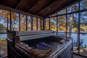 A hot tub with a view of a lake and autumn trees through large windows.