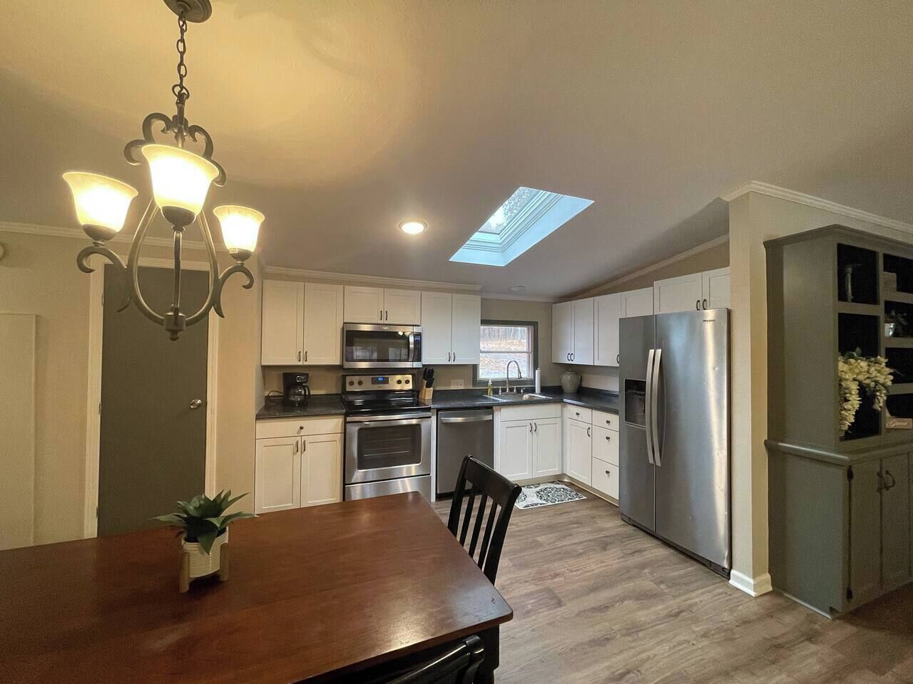 A modern kitchen with white cabinets, stainless steel appliances, and a skylight.