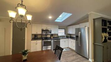 A modern kitchen with white cabinets, stainless steel appliances, and a skylight.