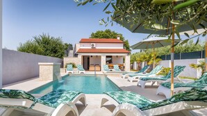 Ein Poolbereich mit Liegestühlen, ein Gebäude mit rotem Ziegeldach und eine Steinmauer.