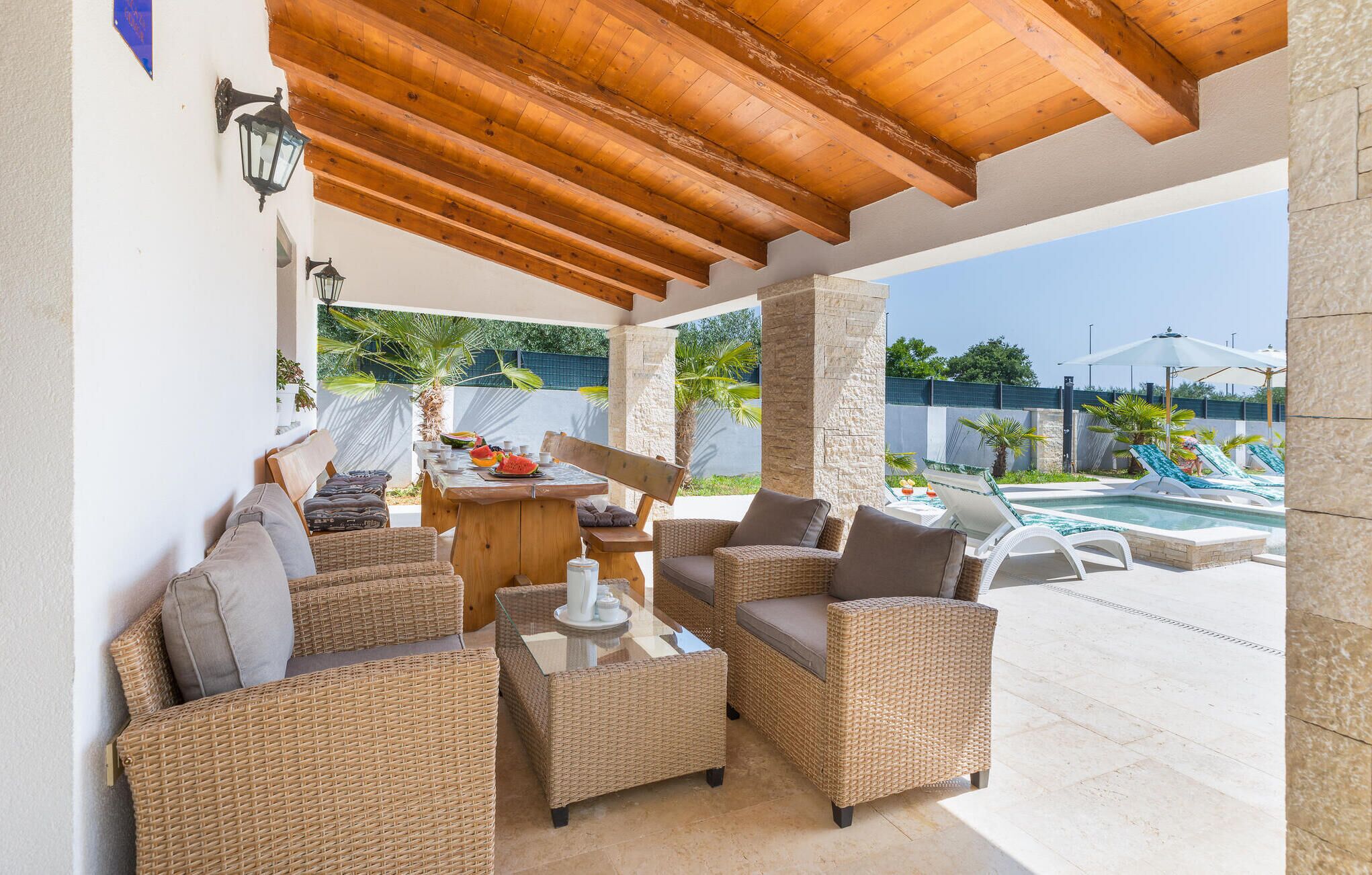 A covered outdoor seating area with wicker furniture, a pool, and a view of the surrounding landscape.