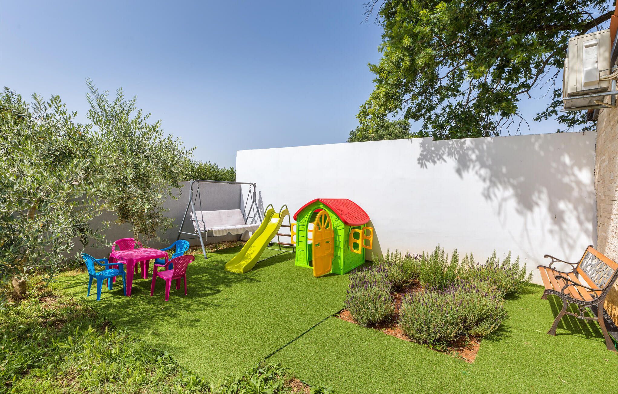 Zona de juegos infantiles con tobogán, columpios y una casita.