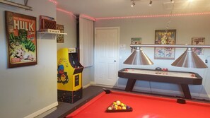 Una habitación con mesa de billar, juegos de arcade y carteles de cómics.