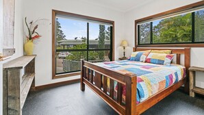 A bedroom with a wooden bed, large windows, a bedside table, and a nightstand.