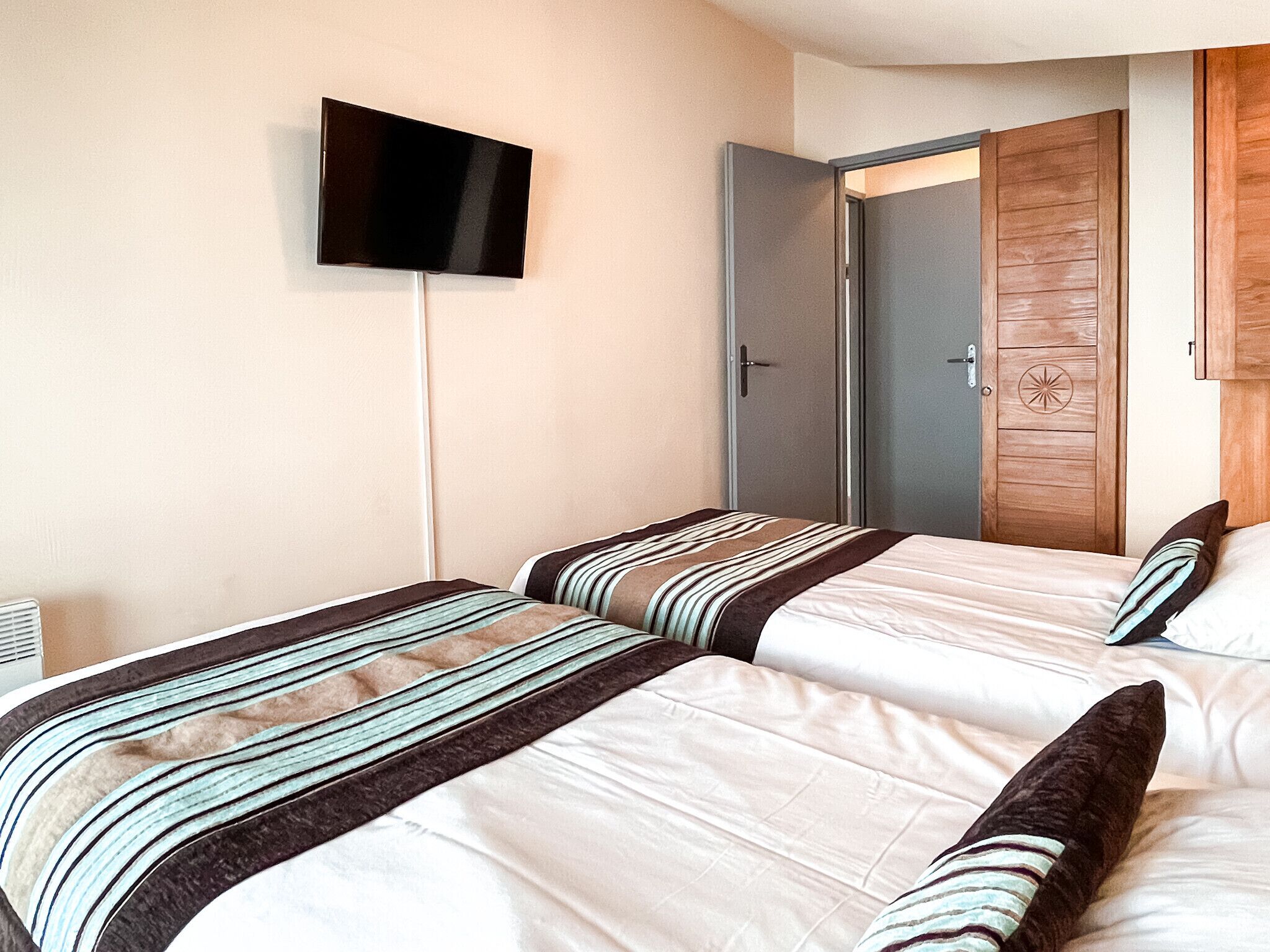 Een hotelkamer met twee bedden, een aan de muur bevestigde televisie en een houten garderobe.