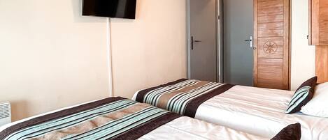 Een hotelkamer met twee bedden, een aan de muur bevestigde televisie en een houten garderobe.