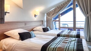 Une chambre d’hôtel avec deux lits, une tête de lit en bois, une table de chevet, une lampe et une vue sur la mer grâce à de grandes fenêtres.