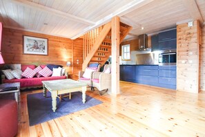 L'interno di una baita in legno con divano, poltrone, un tavolo e un angolo cottura.
