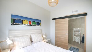 Ein Schlafzimmer mit einem Bett, Nachttischlampen, einem Holzschrank und einem farbenfrohen Bild an der Wand.