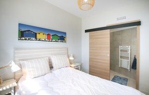 A bedroom with a bed, bedside lamps, a wooden wardrobe, and a colorful painting on the wall.
