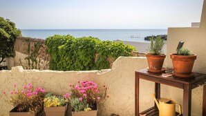 Ein Balkon mit Blumentöpfen, einem Wasserkann und Blick aufs Meer.