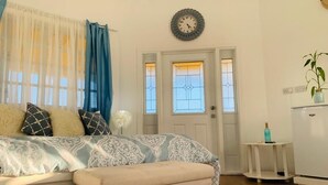 Ein Schlafzimmer mit einem Bett, einem Nachttisch, einer Uhr, einer Tür mit Glasfeldern und einem kleinen Tisch mit einer Pflanze.