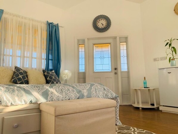 Une chambre à coucher comprenant un lit, une table de chevet, une horloge, une porte avec des panneaux de verre et une petite table sur laquelle est posée une plante.